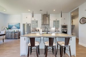 Una cocina moderna con una isla central, iluminación colgante y un comedor con taburetes de bar.