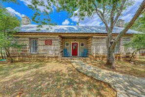 A rustic stone building with a red door, a chimney, and a signboard. - Dog-friendly Cottage on Hwy 290 Wine Trail (Fredericksburg)
