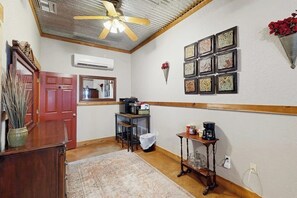 Ein Zimmer mit Deckenventilator, Holzboden, roter Tür, Spiegel, Couchtisch und einer Wand mit gerahmten Bildern.