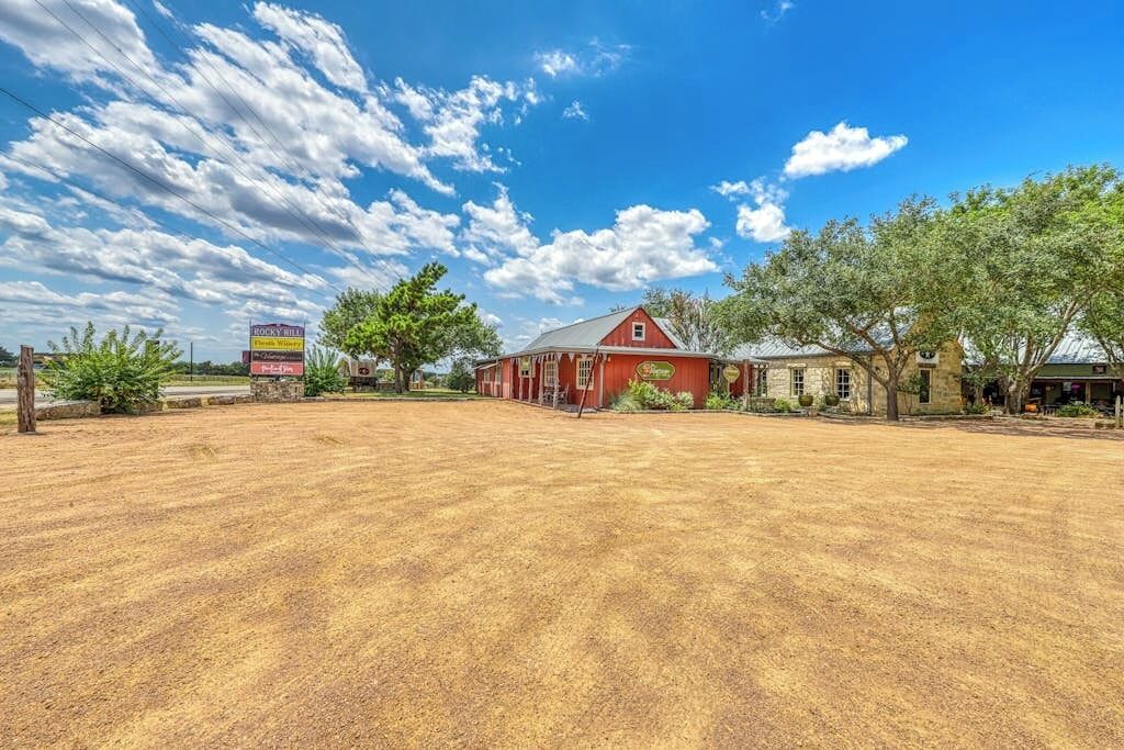 A red barn with a signboard, a stone building, and a clear blue sky with clouds.