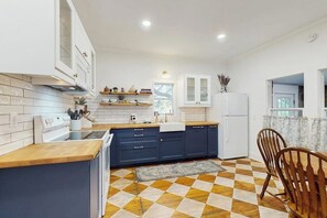 A modern kitchen with a checkered floor, wooden cabinets, and a dining area with chairs. - Blue Haus With Hot Tub, Shuffleboard, EV Charger - Walk to Town & Wineries (Johnson City)