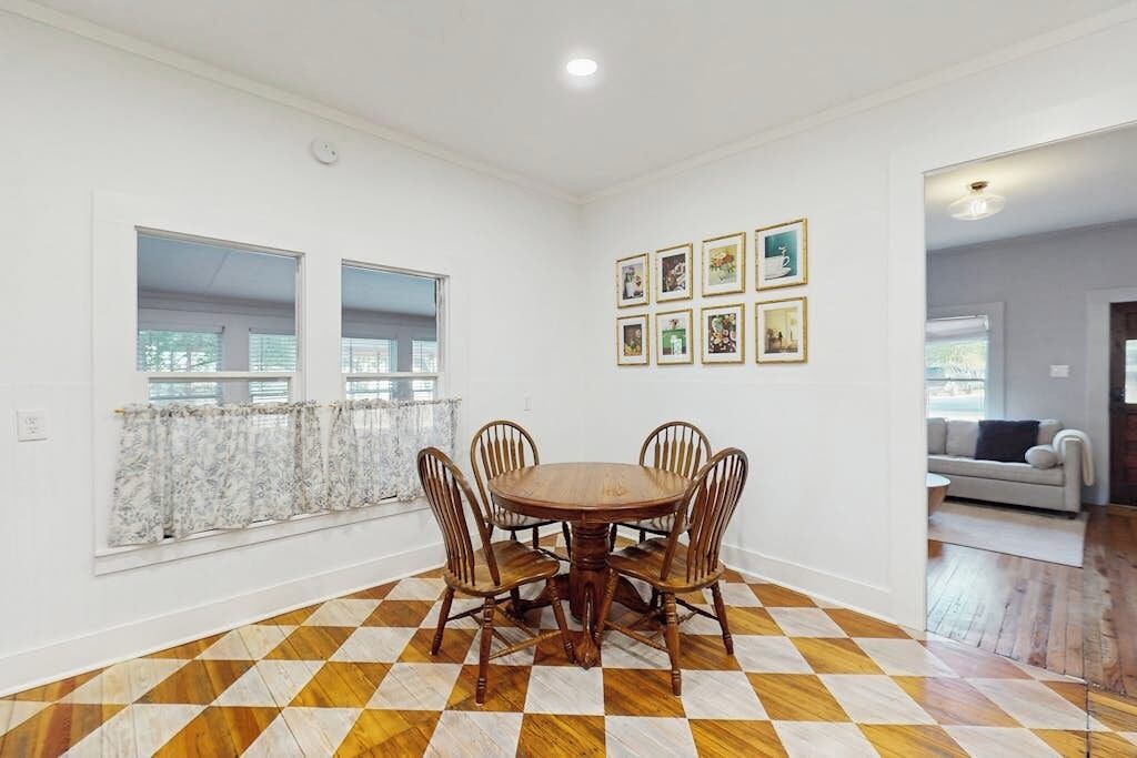 A dining area with a wooden table and chairs, a checkered floor, and a wall with framed pictures.