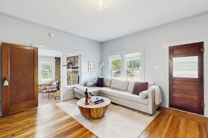 A spacious living room with a large sectional sofa, a round coffee table, and a wooden floor. - Blue Haus With Hot Tub, Shuffleboard, EV Charger - Walk to Town & Wineries (Johnson City)