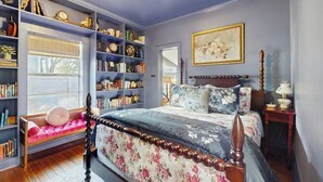 A bedroom with a large bookshelf, a bed with floral bedding, and a painting on the wall. - Blue Haus With Hot Tub, Shuffleboard, EV Charger - Walk to Town & Wineries (Johnson City)