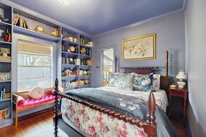 A bedroom with a large bookshelf, a bed with floral bedding, and a painting on the wall. - Blue Haus With Hot Tub, Shuffleboard, EV Charger - Walk to Town & Wineries (Johnson City)