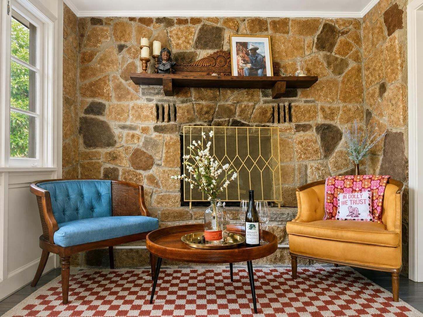 A room with a stone fireplace, two upholstered chairs, a coffee table, and a checkered floor.