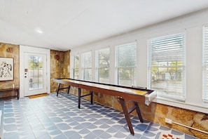 A pool table in a room with a stone wall, a door, and windows with blinds. - Blue Haus With Hot Tub, Shuffleboard, EV Charger - Walk to Town & Wineries (Johnson City)
