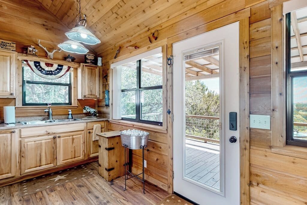 A wooden cabin interior with a kitchen, a door leading to a deck, and a ceiling light fixture.