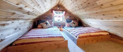 Un dormitorio de buhardilla pequeño con dos camas, una ventana con cortinas y techo de madera.