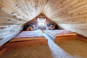 Ein kleines Schlafzimmer im Dachgeschoss mit zwei Betten, einem Vorhangfenster und einer Holzbalkendecke.