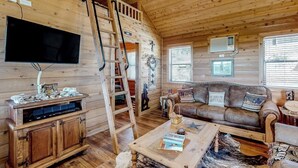 A wooden cabin interior with a TV, wooden furniture, a ladder, a couch, and a ceiling fan. - Amazing Hill Country Cabin With Canyon Views, Furnished Deck, Grill, & AC (Fredericksburg)