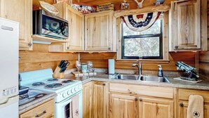 A cabin-style kitchen with wooden cabinets, a stove, a microwave, and a sink. - Amazing Hill Country Cabin With Canyon Views, Furnished Deck, Grill, & AC (Fredericksburg)