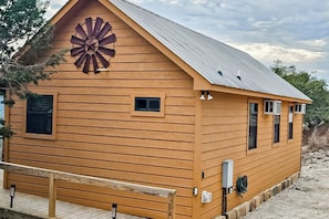 Eine Holzhütte mit einem großen Windrad an der Vorderseite, einem kleinen Fenster und einer Bank davor.
