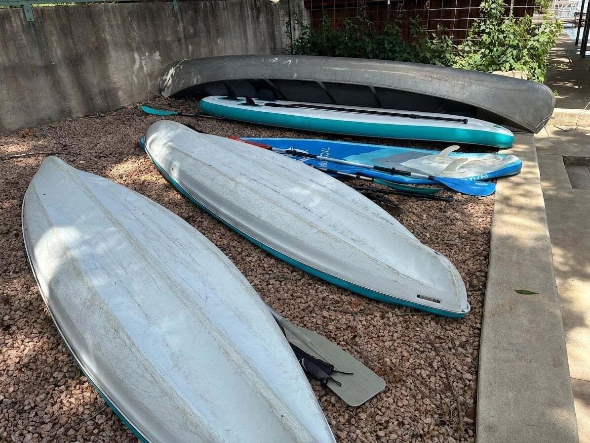 A row of kayaks and paddleboards on a gravel surface.