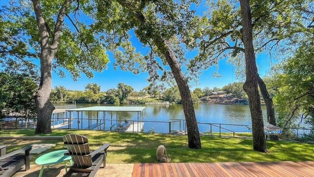 Una terraza de madera con mobiliario exterior, vista a un lago y un área cubierta con barandilla.