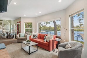 A spacious living room with a red sofa, a grey armchair, and a coffee table. There is a dining area with a table and chairs, and a staircase leading to another level. - Two-story Waterfront Retreat With Boat Dock, Two Firepits & Two Kayaks (Buchanan Dam)
