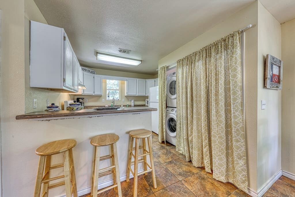 A compact kitchen with a washing machine, a bar area with stools, and a patterned curtain.