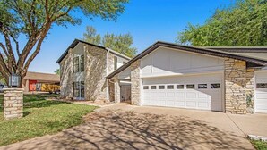 A two-story house with a stone facade, a garage with a white door, and a well-maintained lawn. - Spacious & Elegant Haven With Huge Yard, Updated Interior, AC, & Fast Wifi (Horseshoe Bay)