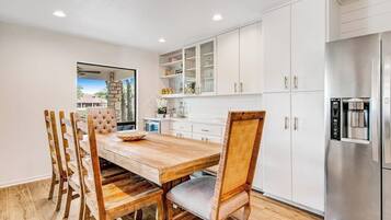 A modern kitchen with white cabinets, a stainless steel refrigerator, and a wooden dining table with chairs.