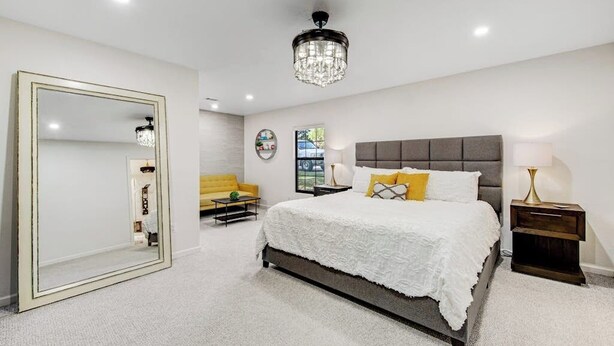 A bedroom with a large mirror, a bed with white bedding, a grey headboard, and a chandelier. - Spacious & Elegant Haven With Huge Yard, Updated Interior, AC, & Fast Wifi (Horseshoe Bay)
