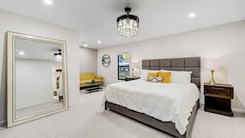 A bedroom with a large mirror, a bed with white bedding, a grey headboard, and a chandelier.