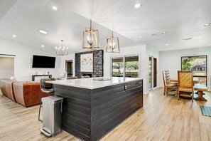 A modern kitchen with a central island, a dining area with a wooden table and chairs, and a seating area with a sofa. - Spacious & Elegant Haven With Huge Yard, Updated Interior, AC, & Fast Wifi (Horseshoe Bay)