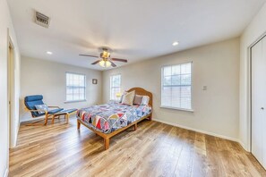 Ein Schlafzimmer mit Holzboden, einem Bett mit bunter Steppdecke, einem Deckenventilator und einem Sessel.