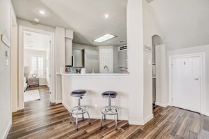 Una cucina con angolo bar, pavimento in legno, pareti bianche e una porta che dà su un'altra stanza.