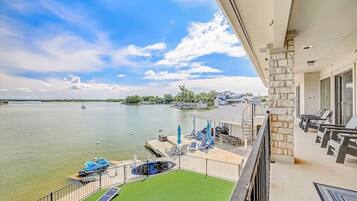 A balcony with a view of a lake, a pool, and a deck area with chairs and umbrellas.