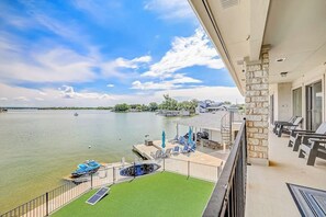 A balcony with a view of a lake, a pool, and a deck area with chairs and umbrellas.