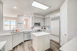 A modern kitchen with white cabinetry, a central island, a microwave, and a refrigerator.