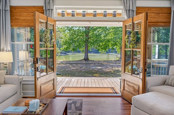 A room with a large wooden door leading to a deck with a view of a lake and trees. - Driftwood Cove Waterfront/Dock/Game house (Miles)