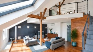 Um loft espaçoso com pé direito alto, vigas de madeira, escada e área de estar moderna com sofás e mesa de centro.