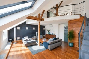 Ein geräumiger Dachboden mit hohen Decken, Holzbalken, einer Treppe und einer modernen Wohnbereiches mit Sofas und einem Couchtisch.