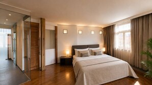 Quarto de hotel moderno com uma cama grande, mesas de cabeceira, porta de vidro que dá para uma varanda e vista da cidade.