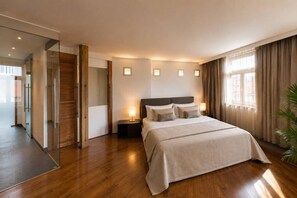 Ein modernes Hotelzimmer mit einem großen Bett, Nachttischen, einer Glastür, die auf einen Balkon führt, und Blick auf die Stadt.