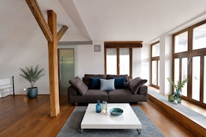 Ein modernes Wohnzimmer mit grauem Sofa, weißem Couchtisch und großen Fenstern.
