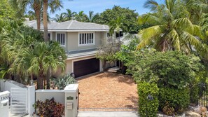 Una casa a due piani con garage, circondata da palme e un giardino curato.
