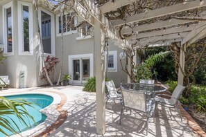 Un'area piscina con una pergola, posti a sedere all'aperto e una casa con ampie finestre.