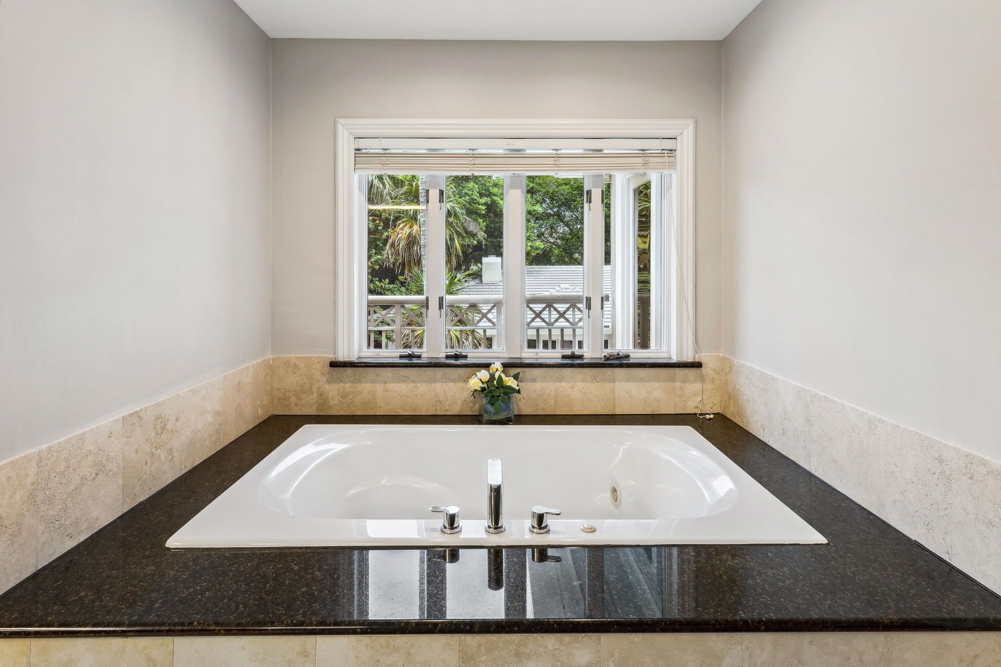 A bathroom with a large white bathtub, a window with a view of greenery, and a small vase with flowers on the counter.