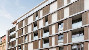 A multi-story building with a modern architectural design, featuring a combination of brick and glass facade, and a parking garage at the ground level. - Central location, 2Bedrooms, Free Parking, Balcony (Prague 5)