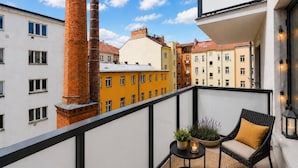 A balcony with a wicker chair, a small table with plants, and a view of colorful buildings and a chimney. - Central location, 2Bedrooms, Free Parking, Balcony (Prague 5)