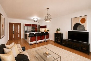 A modern living room with a sofa, a coffee table, a TV, and a kitchen area with a bar. - Central location, 2Bedrooms, Free Parking, Balcony (Prague 5)