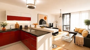 A modern kitchen with red cabinetry, a central island, and a dining area with a sofa and coffee table. - Central location, 2Bedrooms, Free Parking, Balcony (Prague 5)
