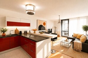 Eine moderne Küche mit roten Schränken, einer zentralen Kochinsel und einem Essbereich mit einer Couch und einem Couchtisch.