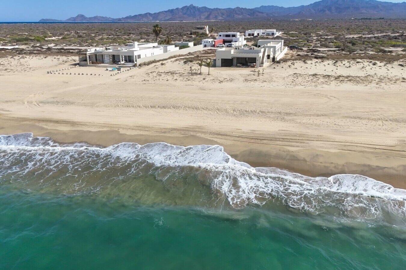 Un hôtel situé sur la côte, composé de plusieurs bâtiments, avec une plage de sable et une vue sur l’océan.