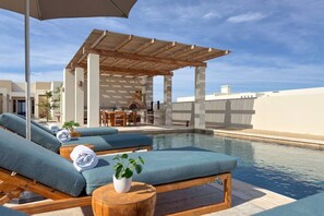 Ein Poolbereich auf dem Dach mit Liegestühlen, einer Holzpergola und einem Essbereich.
