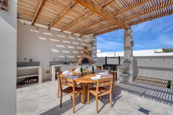 An outdoor dining area with a wooden table and chairs, a grill, and a view of the cityscape.