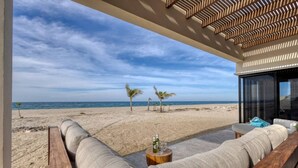 A beachside lounge with a view of the ocean, a wooden bench, and a small table with a bottle. - Oceanfront Luxury in East Cape Private Beachfront (Ligth House Point States)