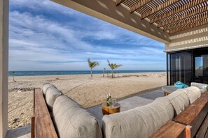 Un salon de plage avec vue sur l’océan, un banc en bois et une petite table avec une bouteille.
